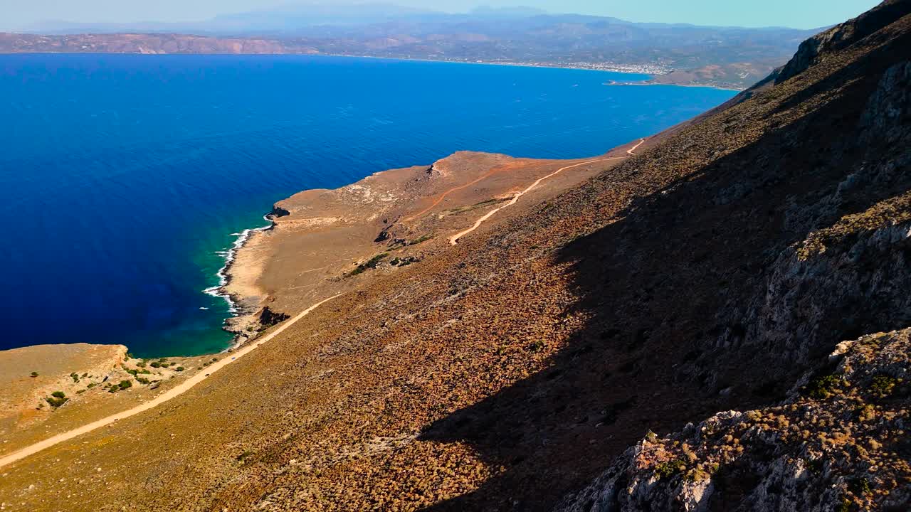 Witness breathtaking views from a cliff in Crete. The clear sunny sky reflects on the vibrant blue sea, revealing the stunning natural beauty of the landscape. Ideal for nature lovers