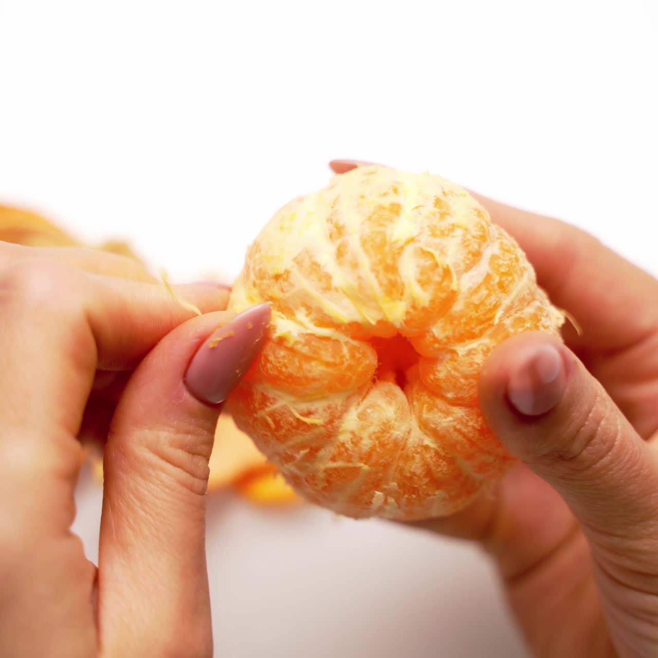 Orange mandarin in woman's hands. Hands are peeling a juicy fruit on white background. Close-up.
