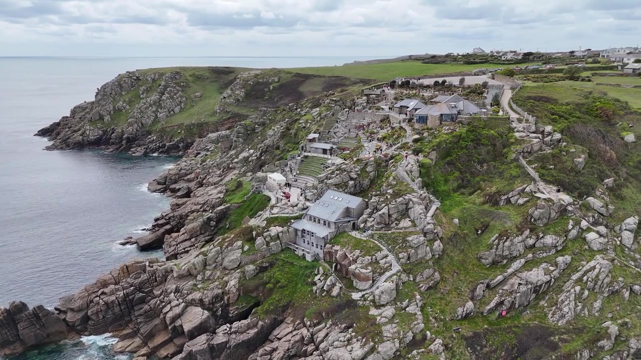 Turkuaz Atlantik sularına ve Cornwall'ın engebeli falezli kıyı şeridine bakan Minack Tiyatrosu'nun sinematik 4K havadan pan çekimi.