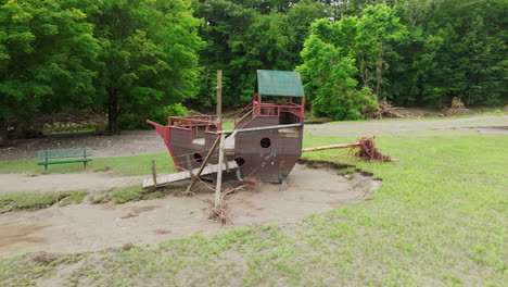 Umlaufende-Luftaufnahme:-Beschädigter-Piratenschiff-Spielplatz-Mit-Baumkollision-Im-Brückenwasser,-Vt