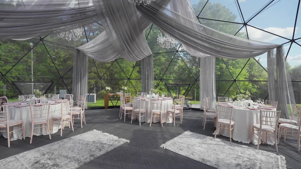 Spacious geodesic dome wedding venue with natural light, draped fabric, crystal chandeliers, and round tables elegantly set. Serene garden view and soft daylight add sophistication. (198 characters)