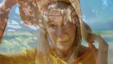 video compuesto de una mujer anciana caucásica con un sombrero sonriendo contra las plantas en el jardín