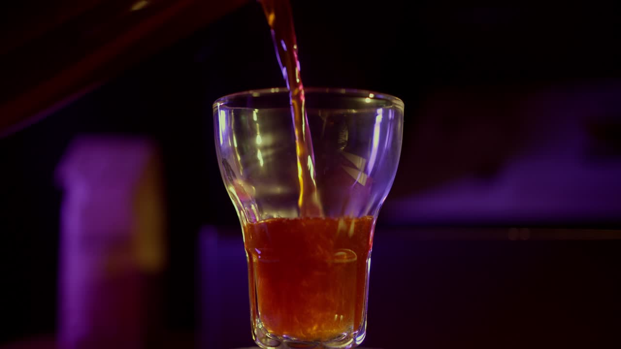 Liquido ambrato che riempie un bicchiere in un'ambientazione scura