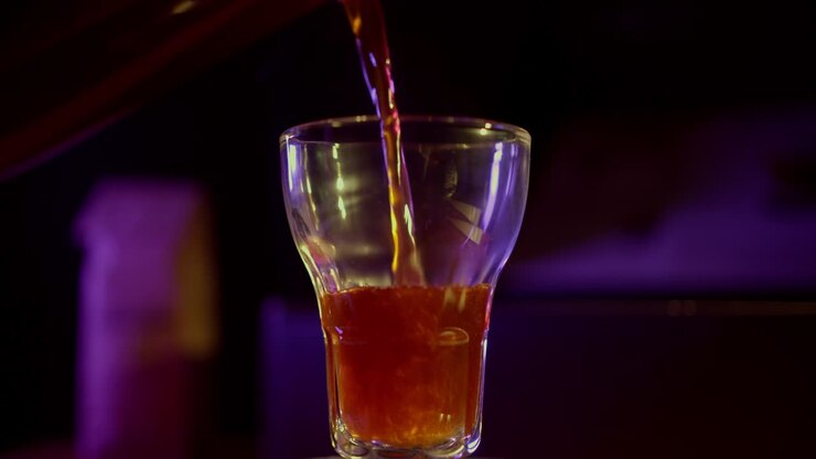 Liquido ambrato che riempie un bicchiere in un'ambientazione scura