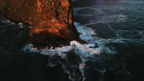 aerial shot of waves crashing against cliff in madeira island at sunrise