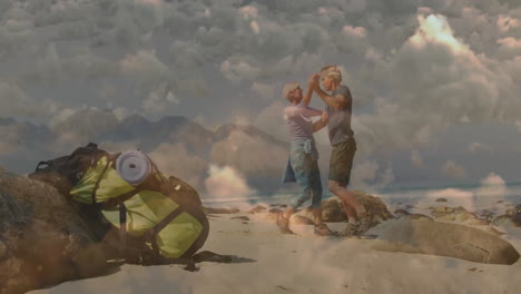 mature couple dancing on rocky beach near backpack and pad, with animated tourism icons floating
