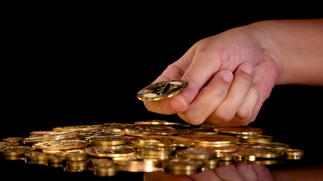 Human hand flips golden digital coin onto stack of coins, dramatic lighting, black background