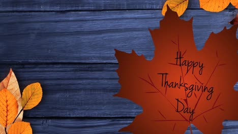 Happy-thanksgiving-day-text-over-autumn-maple-leaf-against-blue-wooden-background