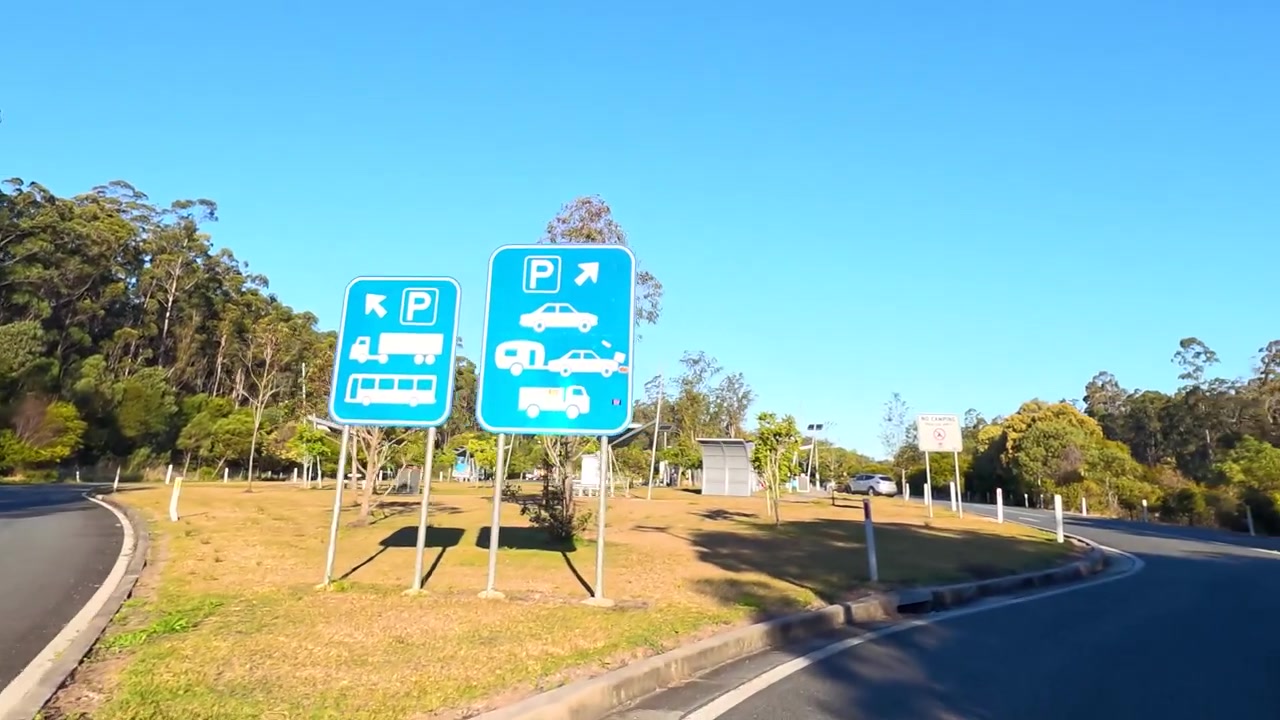 First-person perspective driving into a roadside rest stop under clear blue skies in Australia.