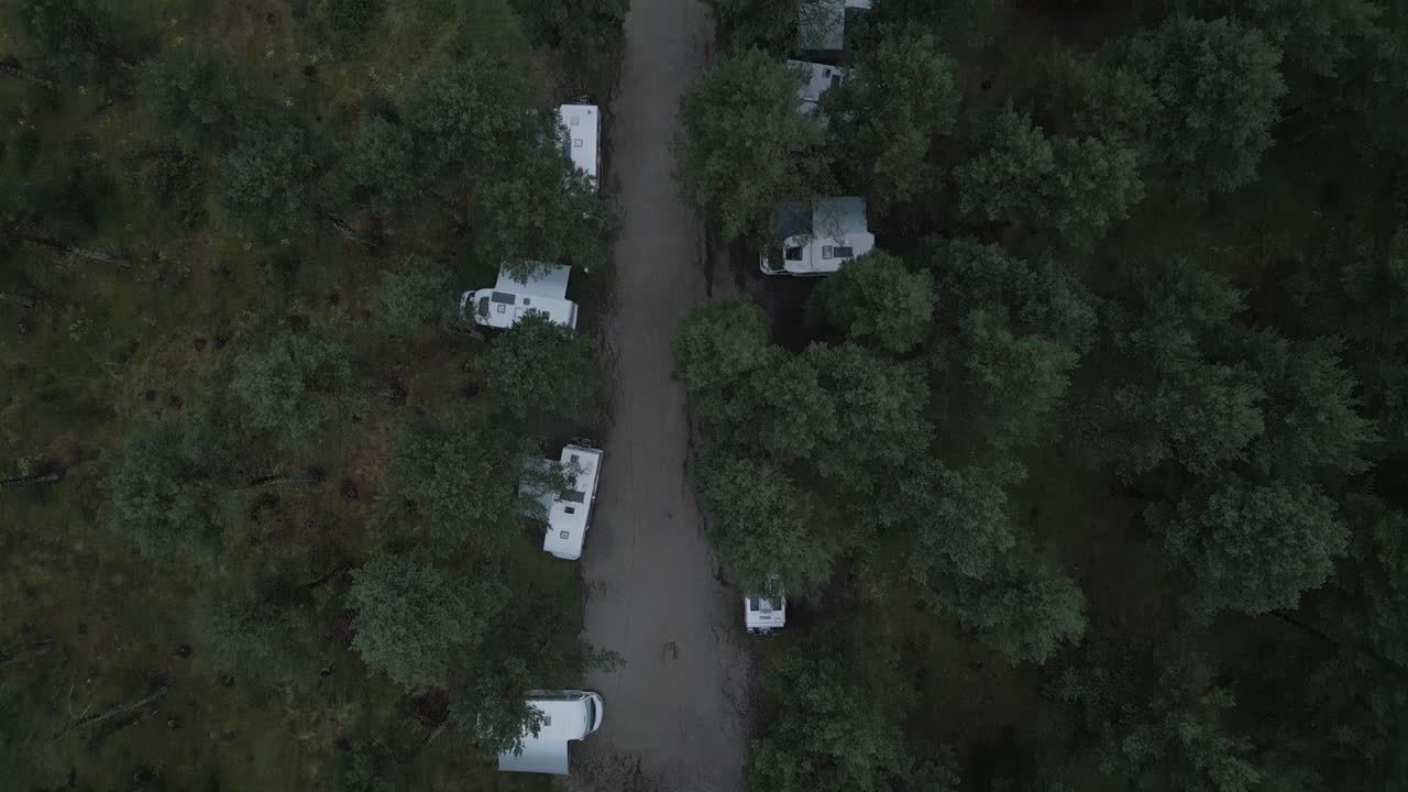 Fransız Pireneleri'ndeki doğal bir kamp alanında, yemyeşil bir çam ormanının altında park edilmiş sıra sıra beyaz kamp minibüsleri ve karavanların yukarıdan çekilmiş havadan çekim görüntüsü