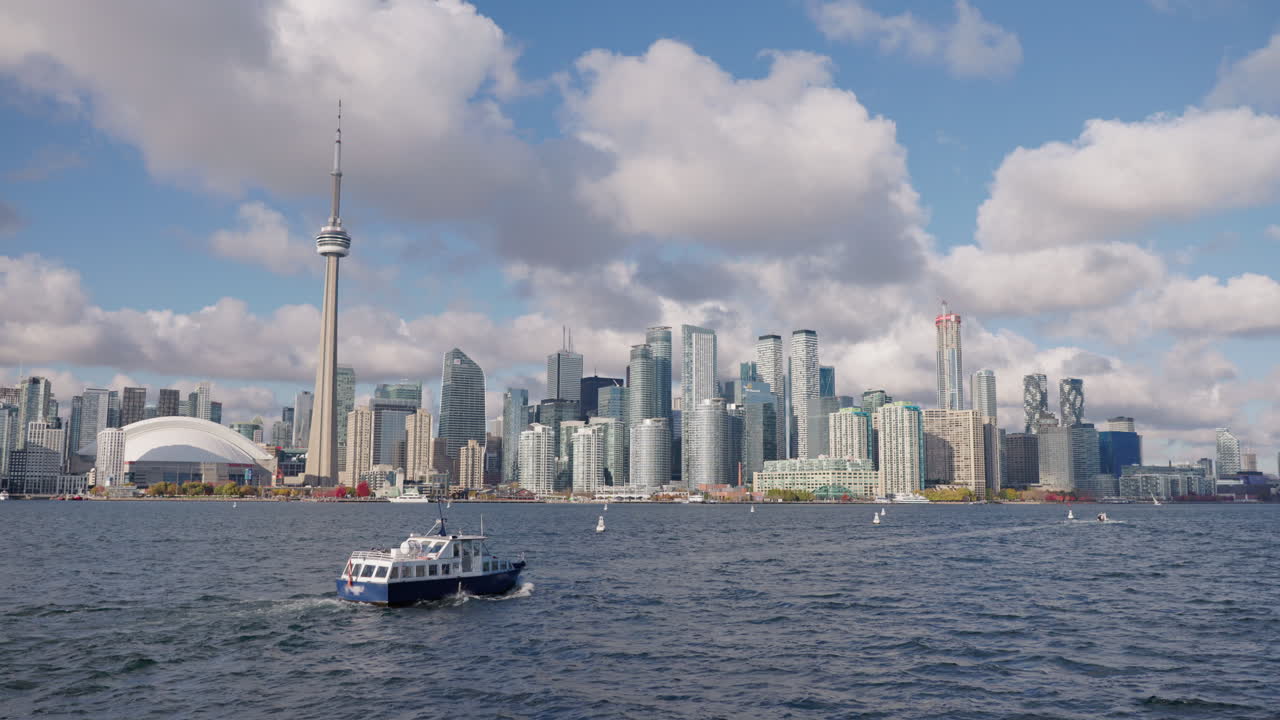 Barca in navigazione sul Lago Ontario con lo skyline di Toronto sullo sfondo, moderno paesaggio urbano con edifici alti e lungomare sotto nuvole imponenti.