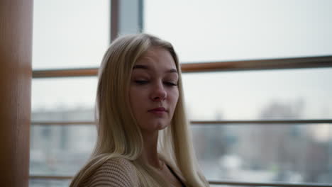 lady in golden woven sweater looking thoughtful in mall while sitting, blurred city view through glass window behind, offering a peaceful and reflective atmosphere, modern urban setting