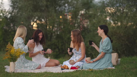 young women after modeling from clay discuss the resulting products drink tea coffee drinks laugh communicate in nature in the open air. creative activity hobbies picnic.