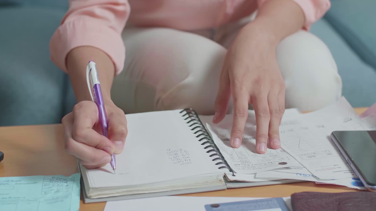 Close Up Of Woman'S Hand Holding The Bill And Recording The Expenses In Notebook