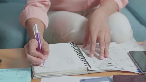 cerca de la mano de la mujer sosteniendo el billete y registrando los gastos en el cuaderno