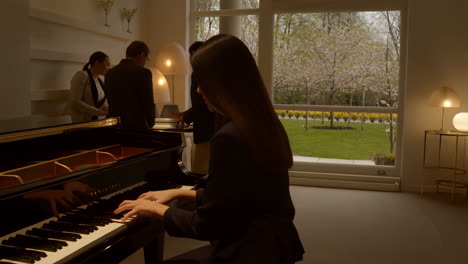 woman playing grand piano in a bright living room with guests and garden view