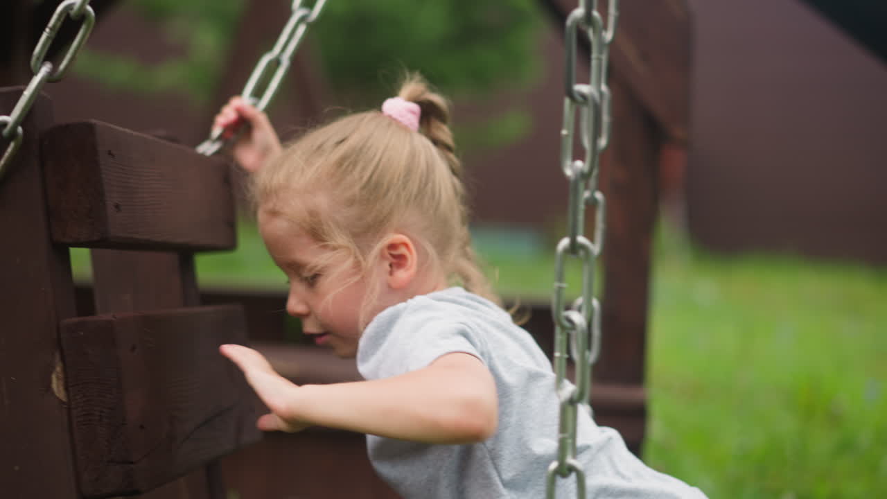 una niña se para de rodillas en columpios de madera en el patio de recreo