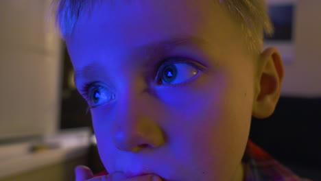 close up of a little boy's illuminated face as he watches tv and eats a snack