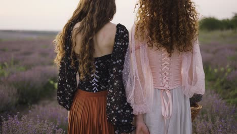 Two-curly-women-are-walking-along-a-lavender,-looking-back-over-shoulder