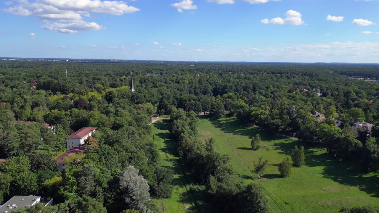 Nikolassee, Berliinin asuinalue, jossa tiheään metsään kätkeytyneitä taloja ja kaupungin siluetti näkyvissä horisontissa. Kaunis ilmakuva, lentopanoraama ja yleiskuva dronella.
