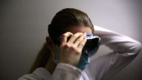 científico-médico de coronavirus que lleva una máscara se aplica gafas de seguridad y mira a la cámara
