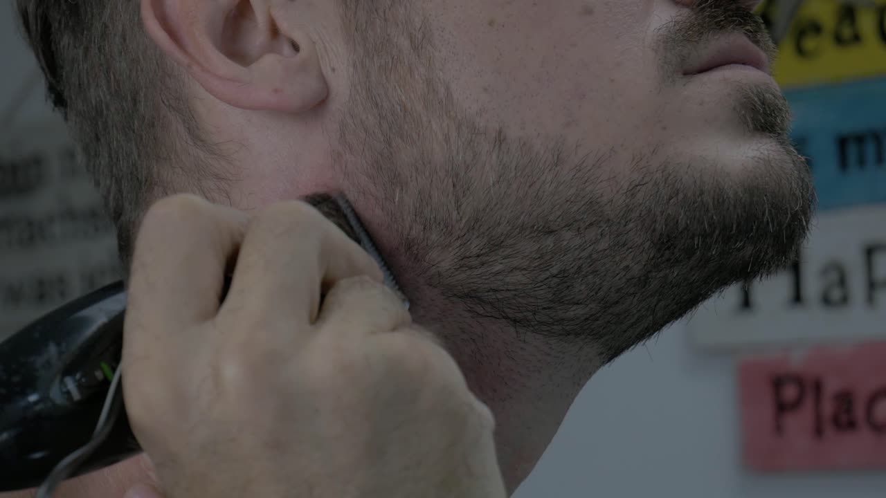 코카시안 남성 이 전기 면도기 로 목 을 면도 하고 있다