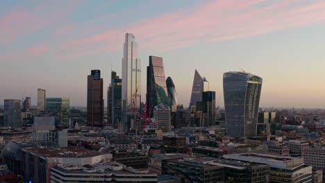 Cinematic-circling-aerial-drone-shot-of-City-of-London-skyscraper-buildings-beautiful-sunrise