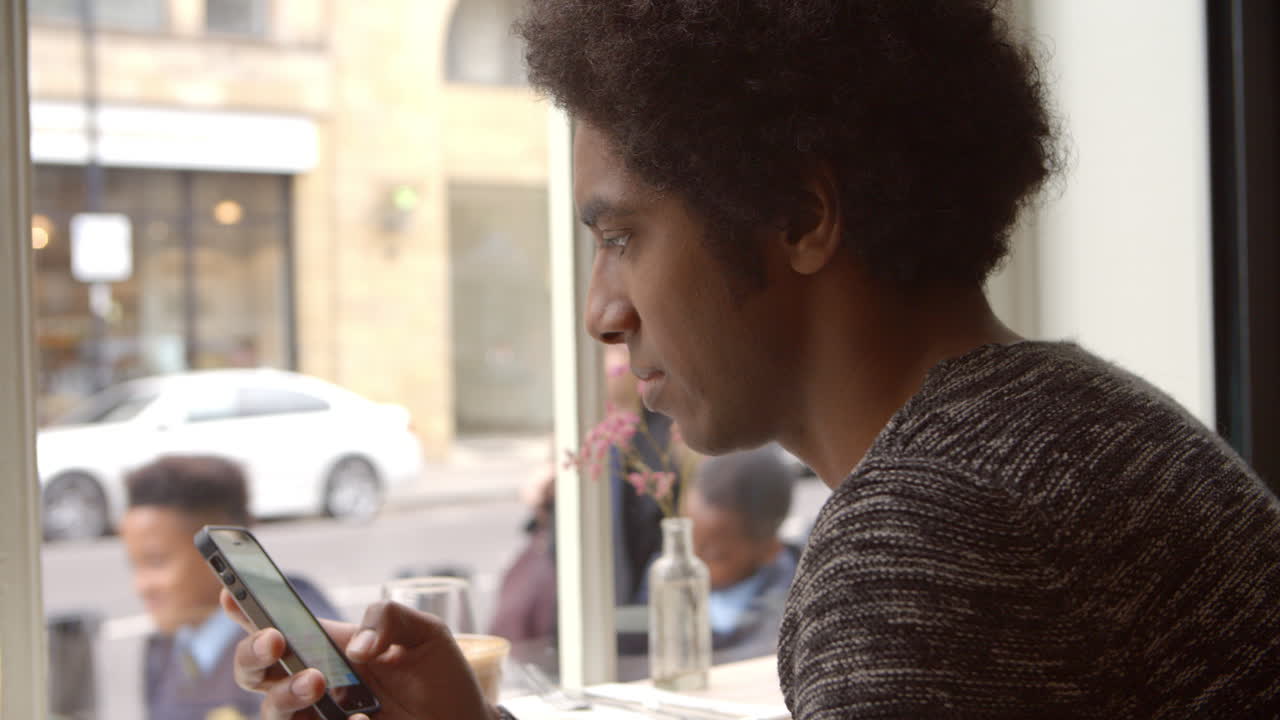 Young Man Using Mobile Phone To Update Social Media In Cafe