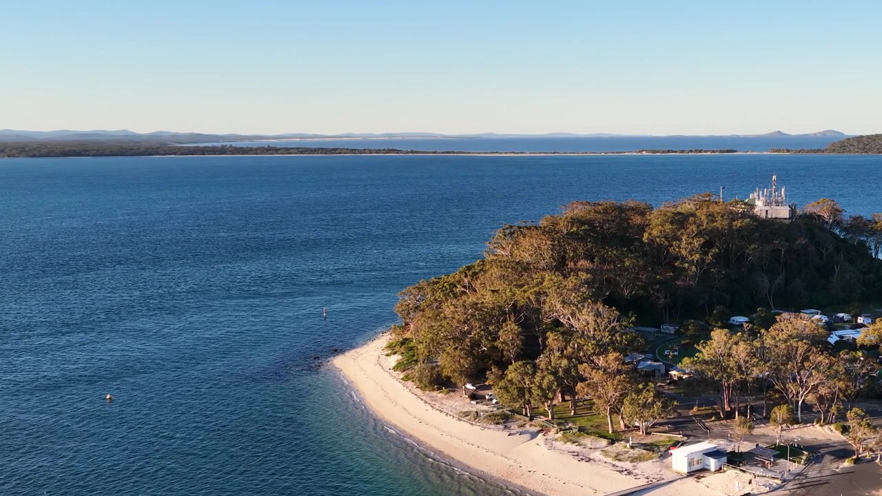 Droneoptagelse fra høj vinkel af et skovklædt forbjerg og en sandstrand i Nelson Bay, Australien