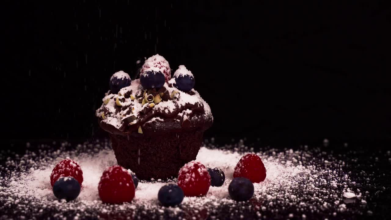 흰 설탕을 가루로 만드는 동안 붉은 과일을 곁들인 초콜릿 머핀의 클로즈업 샷