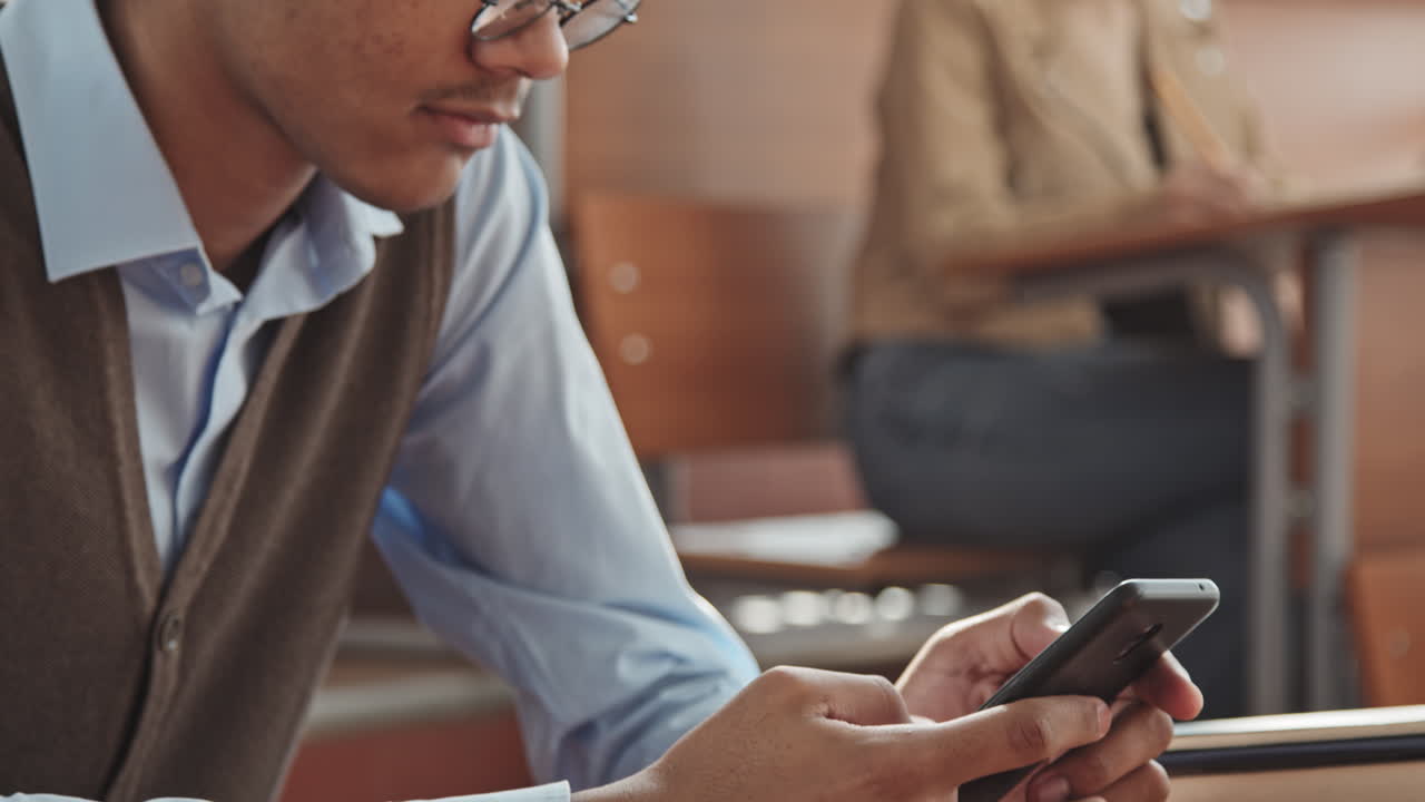 Mixed-Race Student in Earphones Scrolling at Smartphone