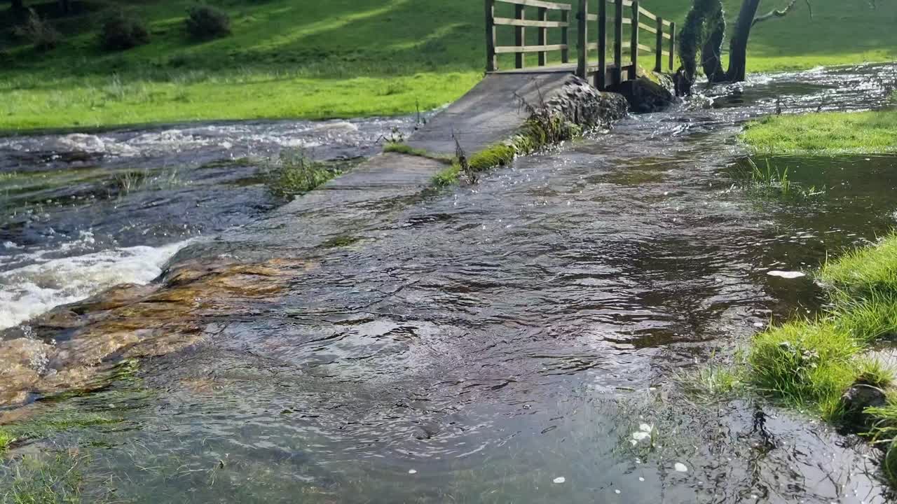 vista de bajo ángulo de la piedra rústica sumergida camino que conduce al puente de madera arqueado desbordando el río inundado