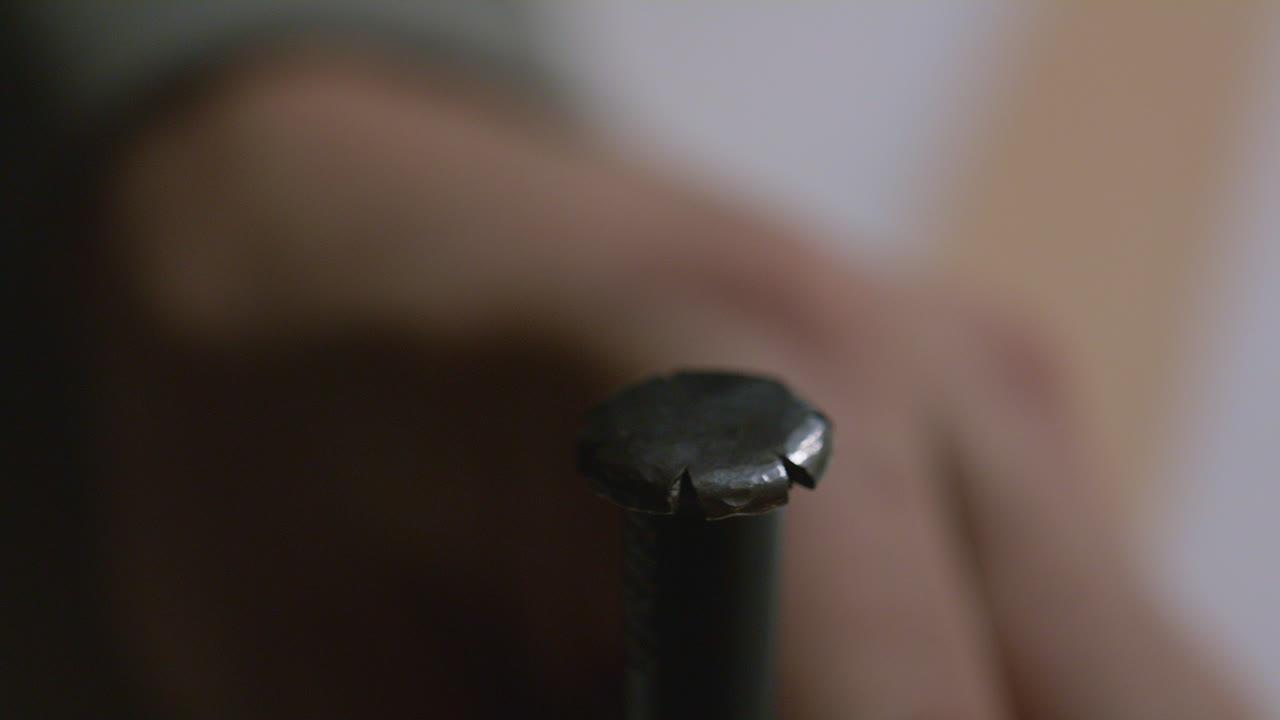 A detailed close-up of a hammer about to strike a leather stamping tool, used for embossing patterns or marks into leather surfaces.