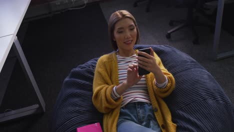 Happy-asian-business-woman-lying-on-bean-bag-using-smartphone-during-break