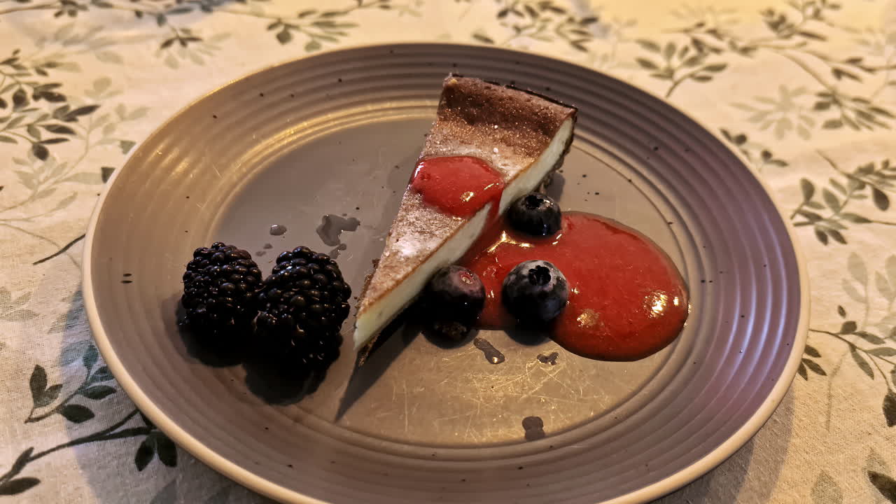 Slice of cheesecake with berries and sauce on a patterned table