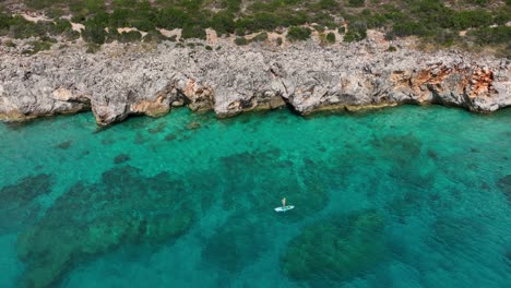 a top-down view captures a person stand-up paddling on the crystal-clear waters of gjipe beach.