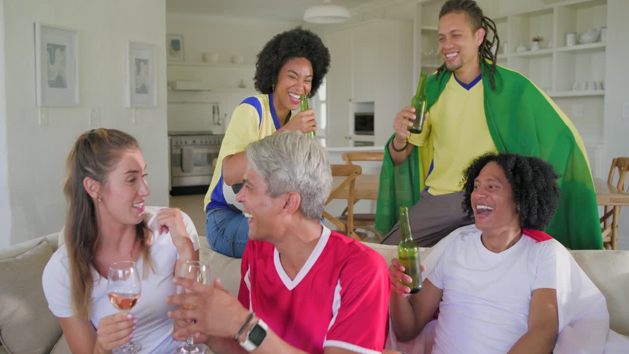 Amigos diversos con camisetas deportivas pasándose botellas de cerveza, sosteniendo un balón de fútbol y reaccionando a un gran gol en el sofá.