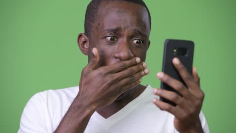 young african man looking shocked while using phone