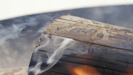 Detail-close-up-of-smoky-burned-wooden-log-with-flames,-outdoor-firepit,-day