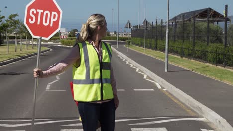 Frau-Mit-Hi-Weste-Hält-Stoppschild,-Während-Mädchen-Roller-Fährt-Und-Die-Straße-überquert