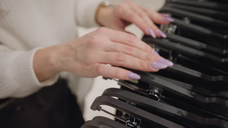 poised shopper with neat manicured nails at high angle browses rows of hangers in softly lit boutique, gracefully shifting through garments to select ideal piece under warm ambient lighting