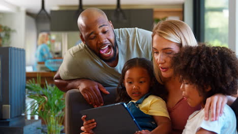 Familia-Con-Tableta-Digital-Haciendo-Muecas-Para-Selfie-En-Casa-Con-Los-Abuelos-En-Segundo-Plano.