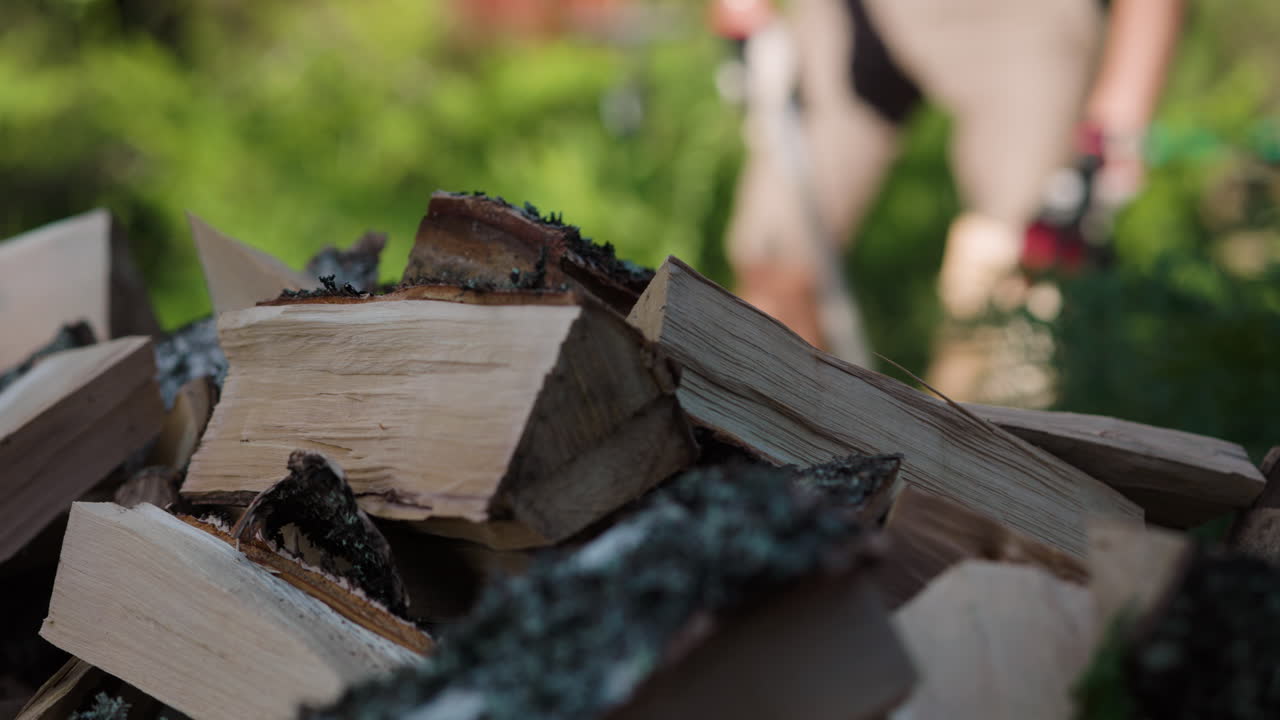 Close pan of pile of firewood as man chops with axe in background