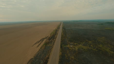 fire-next-to-road,-truck-driving-next-to-smoke-clouds,-farmland-cultivation,-burn-clearing-plantation,-drone-aerial-overview-shot,-roadside-fire,-shot-in-4k