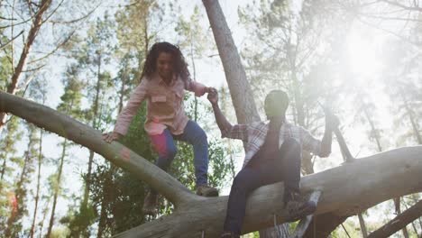 una pareja diversa sonriente tomándose de las manos y sentada en un árbol en el campo