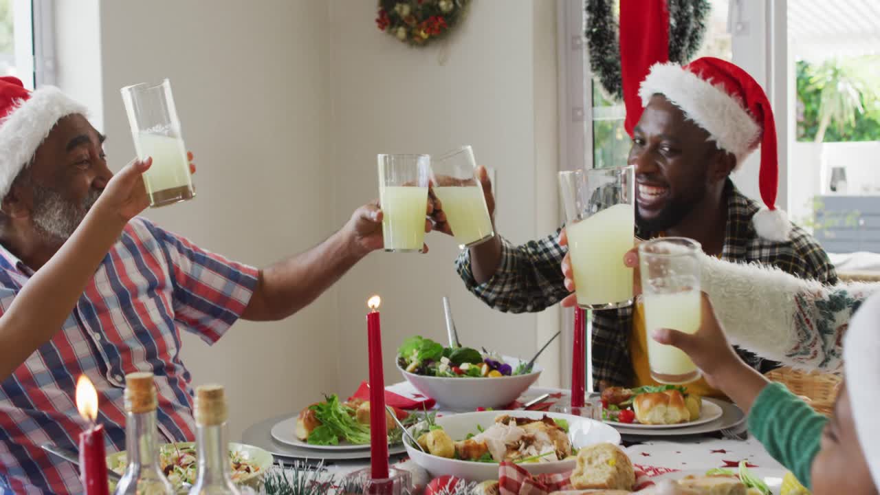 feliz familia afroamericana de varias generaciones con sombreros de papá noel y celebrando la comida navideña