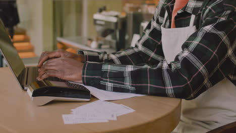 el dueño de la cafetería sentado en la mesa y calculando la factura financiera en una computadora portátil mientras su colega cierra el café