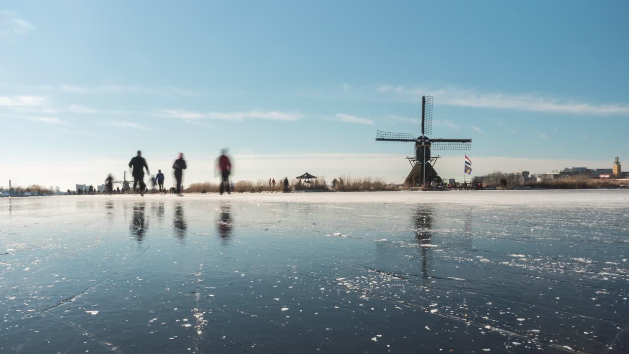 Time lapse of Dutch locals ice skating on frozen canal beside old windmill