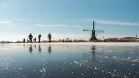 time lapse of dutch locals ice skating on frozen canal beside old windmill