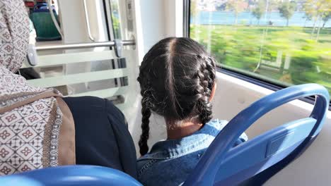child with braids looking out train window